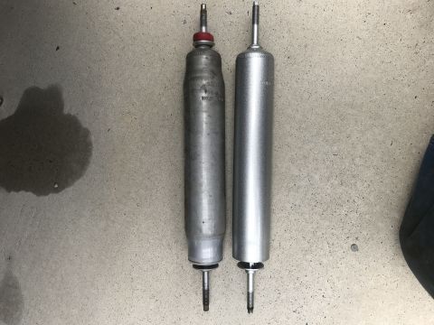 1995 Ford Bronco - Comparison of two shock absorbers, one appearing older and the other newer, resting on a concrete floor.