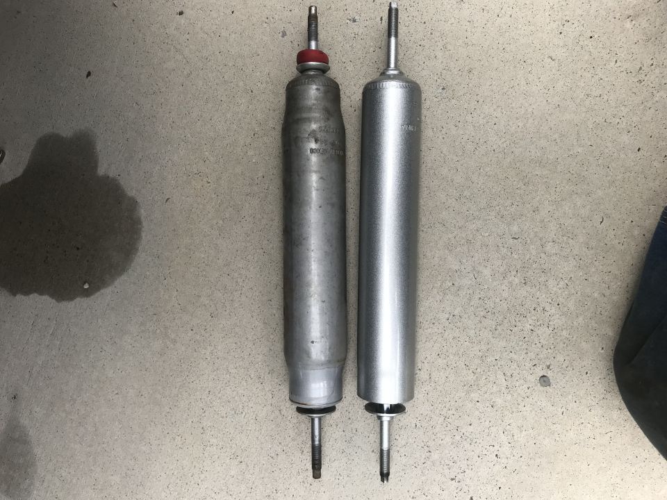 Two shock absorbers, one older and one newer, on a concrete surface