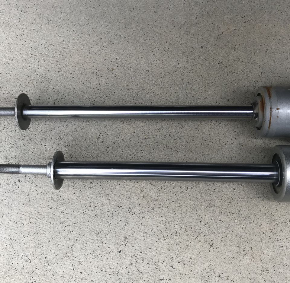 Two shock absorbers with chrome shafts and silver bodies resting on a concrete surface