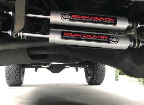 1995 Ford Bronco - Underside view of a vehicle's suspension system, highlighting two Rough Country steering stabilizers and off-road tires.