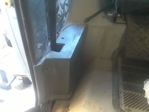 1985 Ford Bronco - The interior of a vehicle's footwell and door jamb area is visible, showing some plastic trim and floor matting.