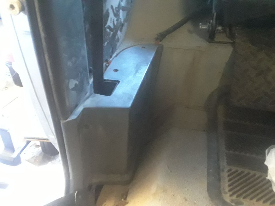 Close-up of the driver's side footwell and door jamb area inside a vehicle. Shows some plastic trim and part of the floor mat
