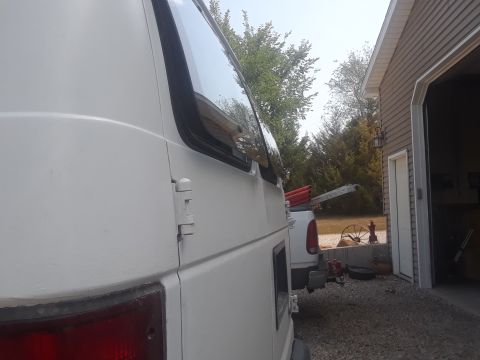 1999 Ford E250 - A white 1999 Ford E250 van is parked next to a garage, with a white pickup truck visible behind it.