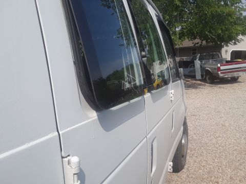 1999 Ford E250 - A white van is parked next to a pickup truck in a gravel lot.