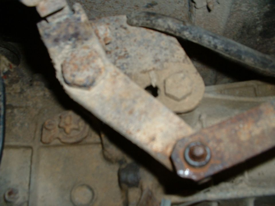 Rusty steel suspension bracket and linkage arm bolted to a chassis crossmember