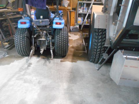 1992 Ford Bronco - A blue tractor is parked indoors next to a large metal trailer with prominent tires.