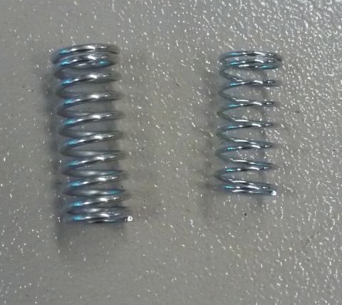 1995 Ford Bronco - Two metal coil springs of different sizes are shown on a gray textured surface.