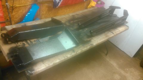 1992 Ford Bronco - Several black painted metal parts, possibly automotive components, are laid out on a workbench. The parts appear to be freshly painted and…