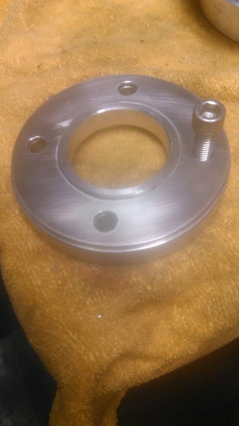 1992 Ford Bronco - A close-up view of a silver metal flange with three bolt holes and one bolt inserted, resting on a textured yellow cloth.