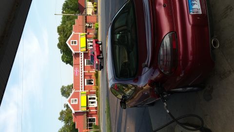 2000 Pontiac Grand Prix - A dark red Pontiac Grand Prix is parked at a gas station, with the gas pump nozzle inserted into the fuel door. The car is viewed from the…