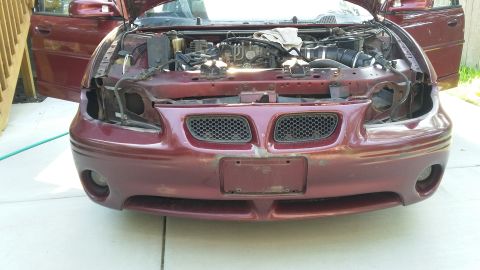 2000 Pontiac Grand Prix - The front of a maroon Pontiac Grand Prix with its hood open, showing the engine bay. The front bumper and grille are visible, and the headl…