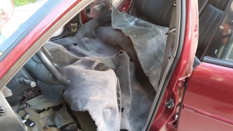 2000 Pontiac Grand Prix - The interior of a red 2000 Pontiac Grand Prix is shown with the driver's side door open and the carpet pulled back, revealing the floor and…