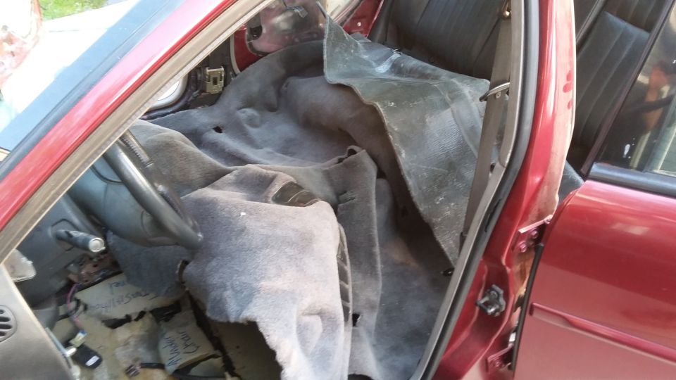 Interior of a red 2000 Pontiac Grand Prix with carpet removed, showing floor and wiring.
