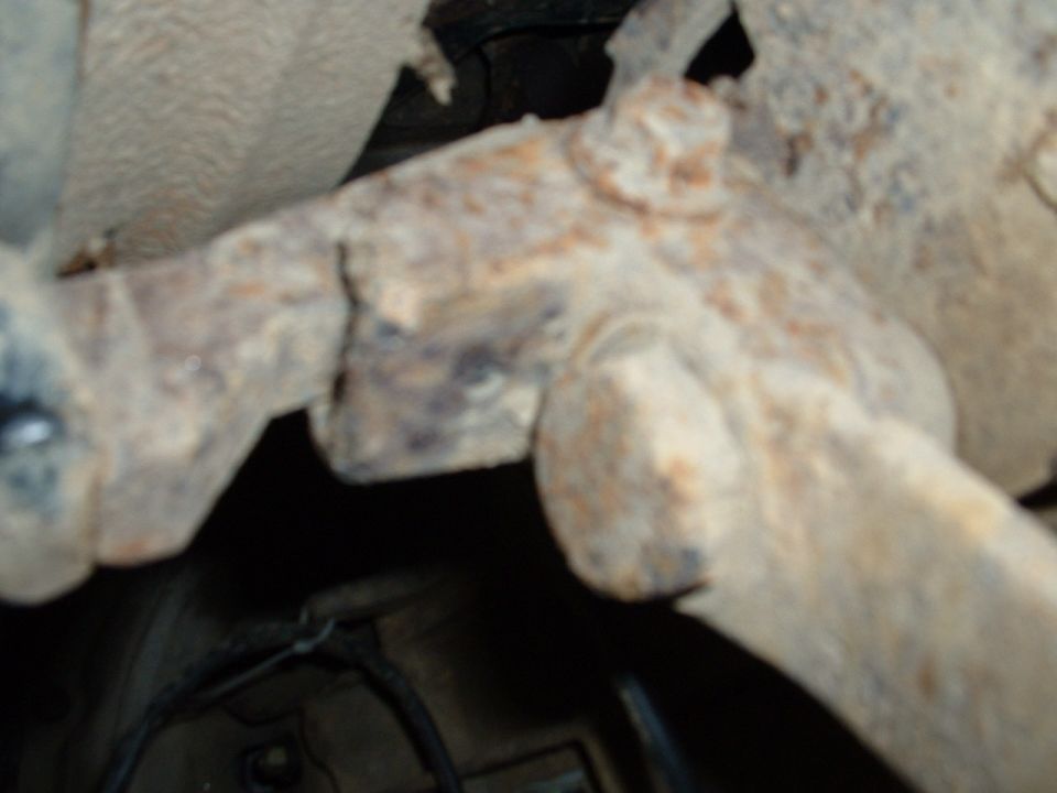Rusty cast steering knuckle and linkage seen in a close-up underbody flash photo