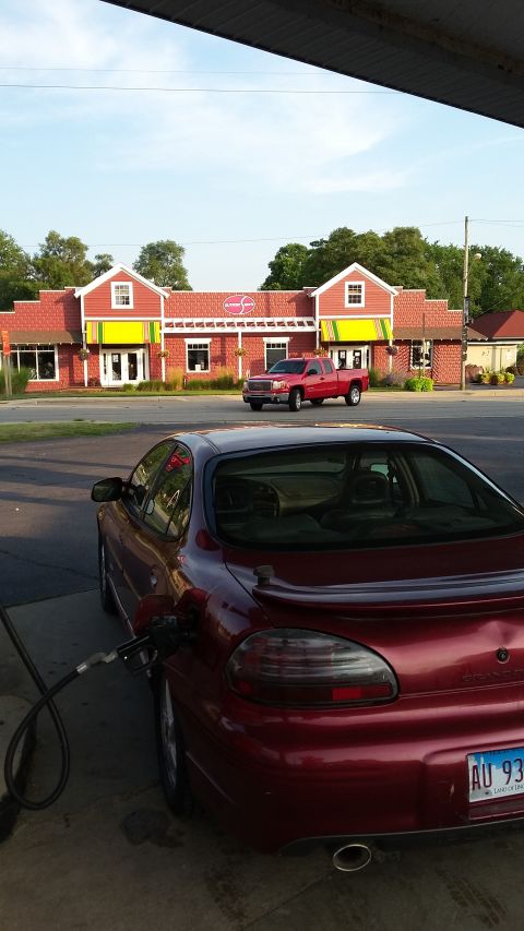 2000 Pontiac Grand Prix - A dark red 2000 Pontiac Grand Prix is parked at a gas station, with the fuel nozzle inserted into the gas tank. A red pickup truck is visib…