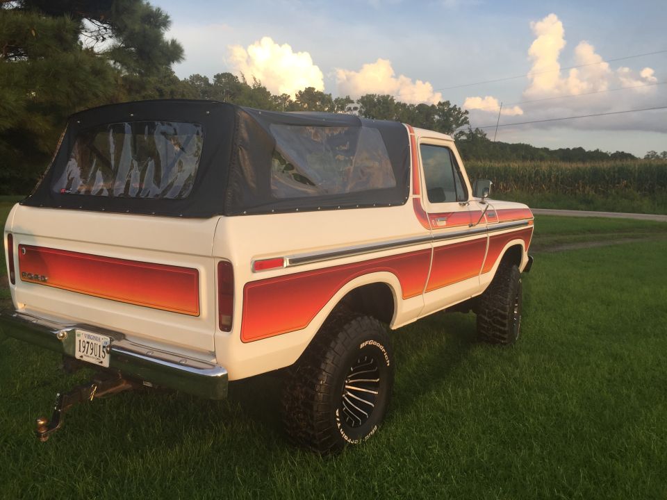 1979 Ford Bronco with soft top, white with orange/red decals, parked on grass.