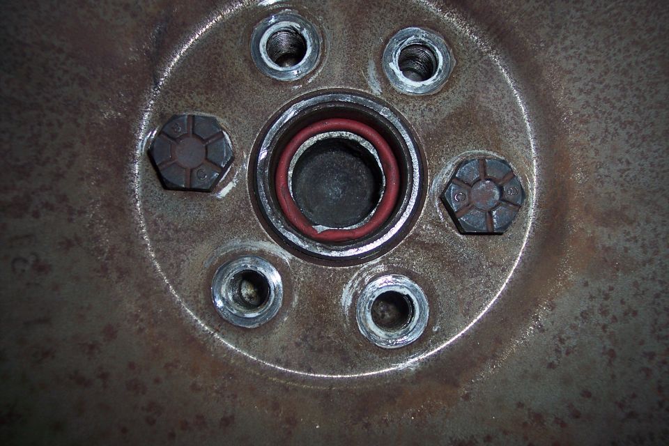 Rusty metal flywheel with bolts and a red gasket.