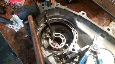 1985 Ford Bronco - A close-up view of a transmission or transfer case assembly with internal gears and a bearing visible. Tools including a rubber mallet, a s…