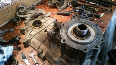 1985 Ford Bronco - A close-up view of disassembled transmission or transfer case components laid out on a wooden workbench. Various metal parts, tools, and a…