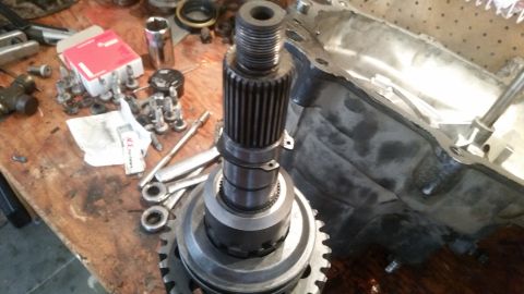 1985 Ford Bronco - A close-up view of a transmission input shaft and gear assembly resting on a wooden workbench next to transmission parts and tools.