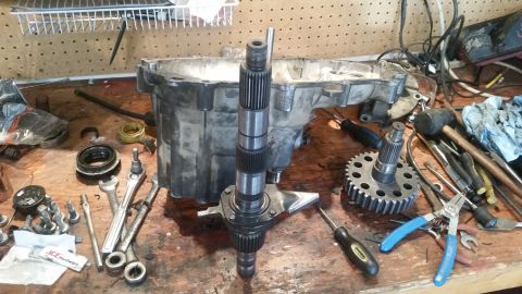 1985 Ford Bronco - A workbench displays disassembled transmission parts including a large aluminum casing, a splined shaft, and a large gear. Various tools li…