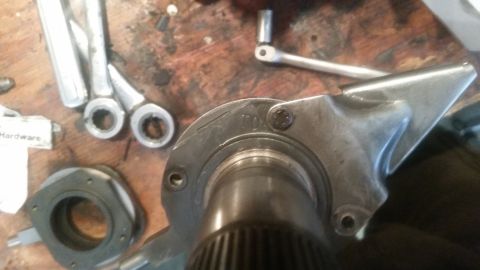 1985 Ford Bronco - A close-up view of a metal automotive part with stamped markings and a bolt. Tools and other parts are visible in the blurred background on…