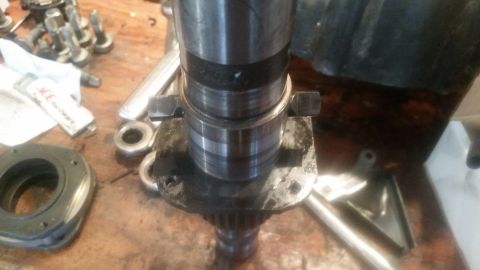 1985 Ford Bronco - A close-up view of a metal shaft with a bearing assembly and two bolts securing it to a flange. Various other metal parts and a tube of har…