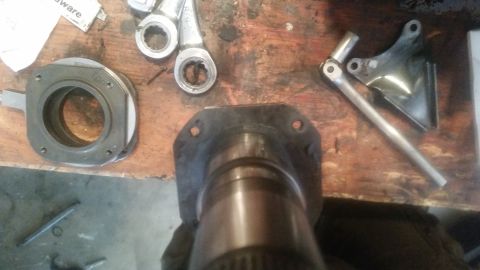 1985 Ford Bronco - A collection of automotive parts, including a bearing housing labeled "Top", a metal bracket, and a shaft with a flange, are laid out on a…