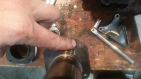 1985 Ford Bronco - A hand points to a gasket with two bolt holes, positioned on top of a metal component with a bearing. A ratchet and socket are visible on a…