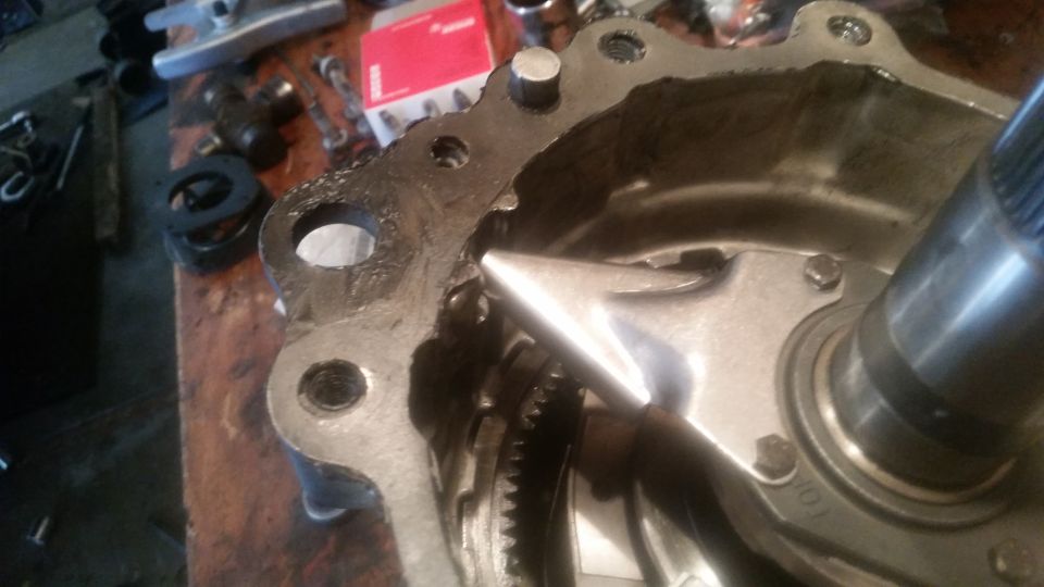 Damaged metal housing with visible gear inside, likely part of a vehicle drivetrain.