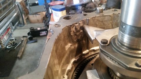 1985 Ford Bronco - Close-up view of a damaged metal transmission housing with visible welding repairs. A gear and part of a shaft are visible inside the housi…