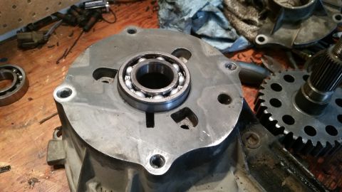 1985 Ford Bronco - A close-up view shows a metal casing with a bearing installed in the center. Various mechanical parts and tools are scattered on a wooden w…