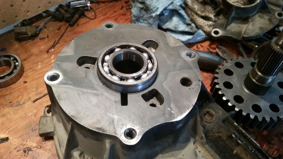 Close-up of a metal casing with a bearing installed, on a wooden workbench with other parts.