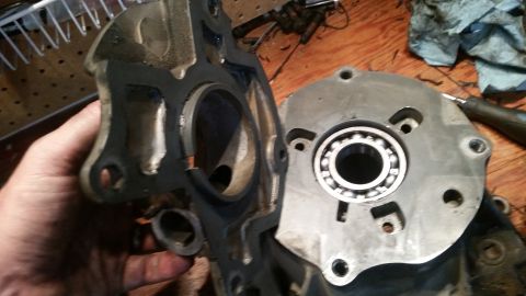 1985 Ford Bronco - A hand holds a disassembled metal engine component with a bearing visible in the right-hand piece. The parts are on a wooden workbench with…