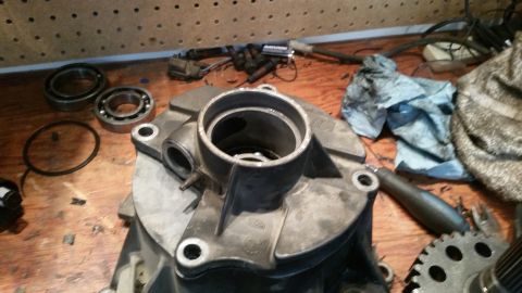 1985 Ford Bronco - A close-up view of vehicle parts, including bearings, a gasket, and a transmission housing, laid out on a wooden workbench.