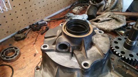 1985 Ford Bronco - A close-up view of a disassembled automotive transmission or differential housing with a bearing and gear visible on a wooden workbench. Va…