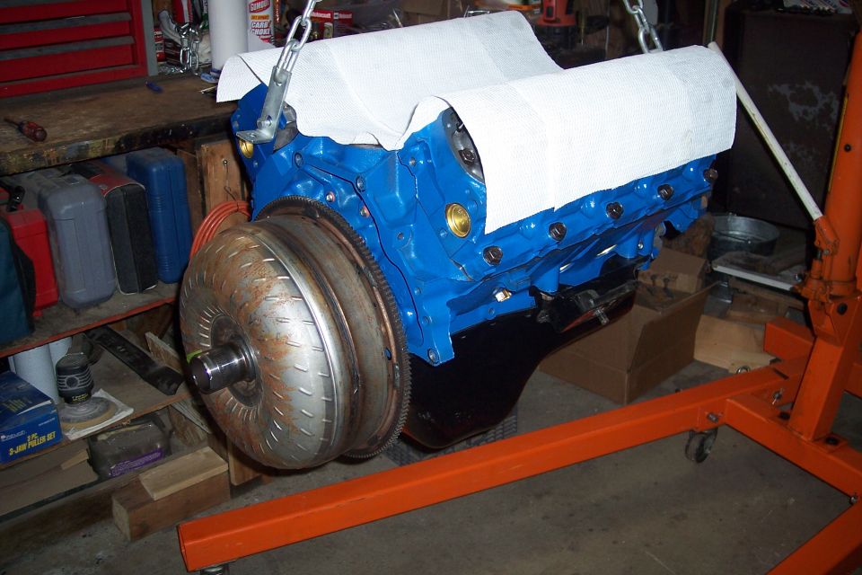 Blue V8 engine with torque converter on an engine stand, covered with paper towels.