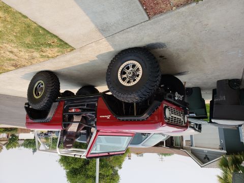 1968 Ford Bronco - A red 1968 Ford Bronco with large off-road tires is parked on a concrete driveway next to a sidewalk and grass. The vehicle has a roll cage…
