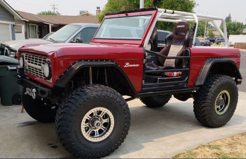 1968 Ford Bronco - A modified red 1968 Ford Bronco is parked on a concrete driveway in front of a house. The vehicle features large off-road tires, a roll cag…