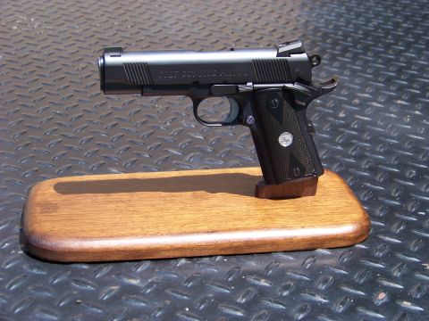 1995 Mercury Grand Marquis - A black Colt 1911 pistol is displayed on a wooden stand against a textured dark background.