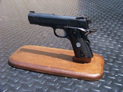 1995 Mercury Grand Marquis - A black semi-automatic pistol is displayed on a wooden base, which is placed on a diamond plate surface.