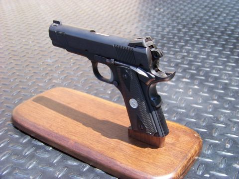 1995 Mercury Grand Marquis - A black semi-automatic pistol is displayed on a wooden stand against a textured metallic background.