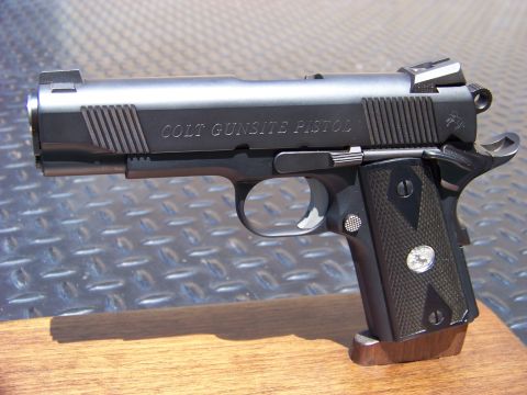 1995 Mercury Grand Marquis - A close-up, side profile of a black Colt Gunsite Pistol is displayed on a wooden surface with a diamond plate metal background.