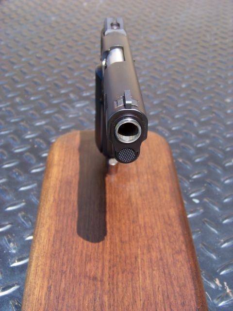1995 Mercury Grand Marquis - A close-up, head-on view of the muzzle and front sight of a dark-colored handgun resting on a wooden stand. The handgun is positioned on a…