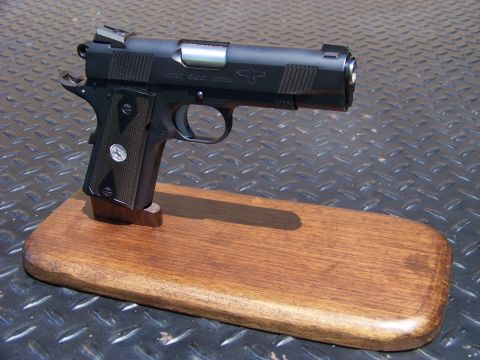 1995 Mercury Grand Marquis - A black Colt C.C.C. Model pistol is displayed on a wooden stand. The pistol is resting on a textured metal surface.