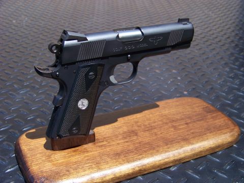 1995 Mercury Grand Marquis - A black semi-automatic pistol with textured grips is displayed on a wooden stand. The pistol has "COLT G.C.O. MODEL" and a horse logo engra…