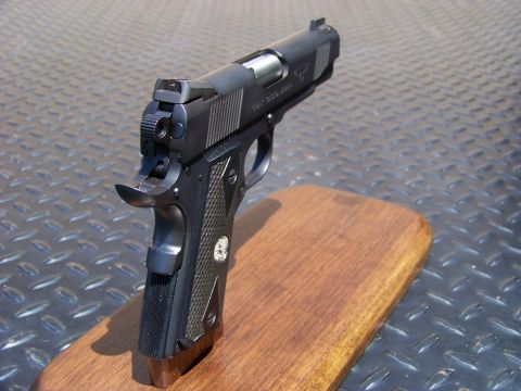1995 Mercury Grand Marquis - A black semi-automatic pistol with checkered grips rests on a wooden block against a diamond plate background.
