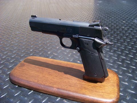 1995 Mercury Grand Marquis - A black semi-automatic pistol is displayed on a wooden stand against a textured metal background.