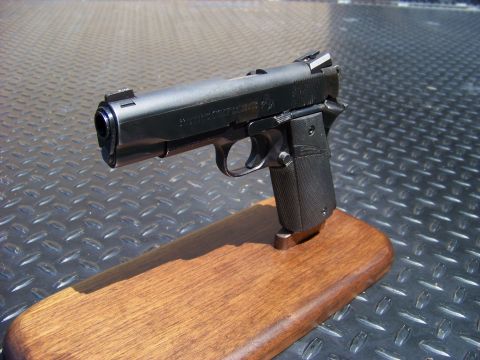 1995 Mercury Grand Marquis - A black semi-automatic pistol is displayed on a wooden stand. The pistol is resting on a textured metal surface.