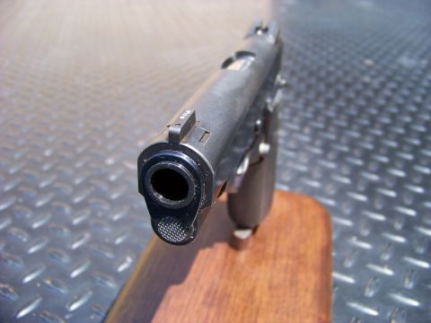 1995 Mercury Grand Marquis - The image shows a close-up, head-on view of the barrel and front sight of a handgun resting on a wooden stand. The handgun is dark colored…